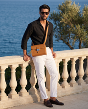 Le Messager Brun doré porté en bandoulière, pantalon blanc et chemise noire, au bord de la mer