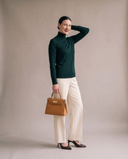 La Duchesse coloris camel portée à la main par l'égérie La Firkin, pull vert sapin et pantalon crème