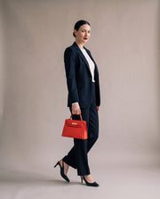 La Duchesse coloris rouge portée à la main par l'égérie La Firkin, blazer et pantalon marine