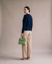 La Duchesse coloris vert avocat portée à la main par l'égérie La Firkin, pull marine et pantalon sable, vue de trois quarts dos