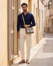 Le Messager Gris éléphant porté en bandoulière, polo en maille marine et pantalon crème, dans une ruelle ensoleillée