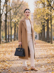 Le Firkin en cuir pleine fleur coloris Onyx noir, boucle dorée, porté à la main avec un manteau camel
