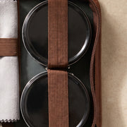 Détail de la trousse d'entretien du cuir La Firkin : cirage noir et crème neutre sous leurs bandes élastiques